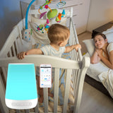 White noise machine placed on baby crib with mobile app screen showing sound and light controls.