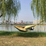 Lightweight camping hammock set up between trees by the lake